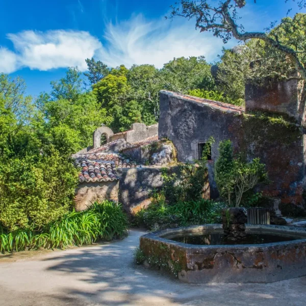 Patio del Convento dos Capuchos con una fuente de piedra y edificios rodeados de vegetación en Sintra.