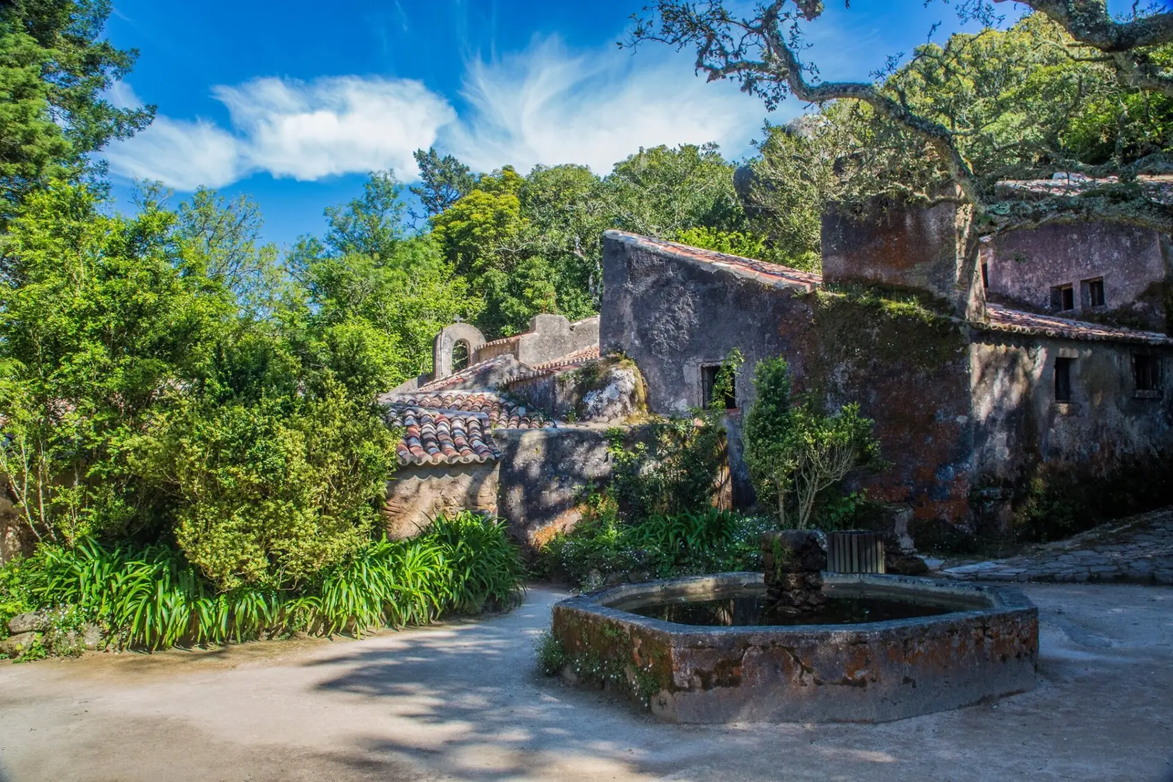 Patio del Convento dos Capuchos con una fuente de piedra y edificios rodeados de vegetación en Sintra.