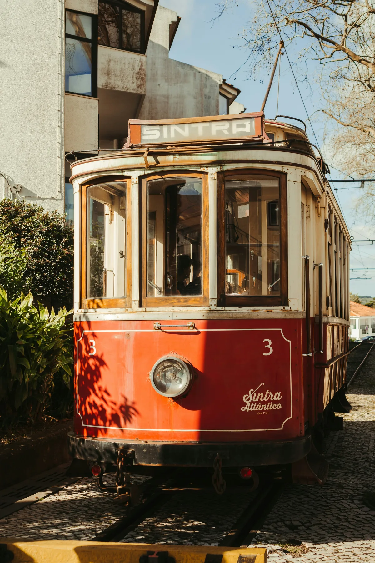 Tranvía histórico rojo de Sintra, con el número 3, detenido sobre las vías entre edificios y vegetación.