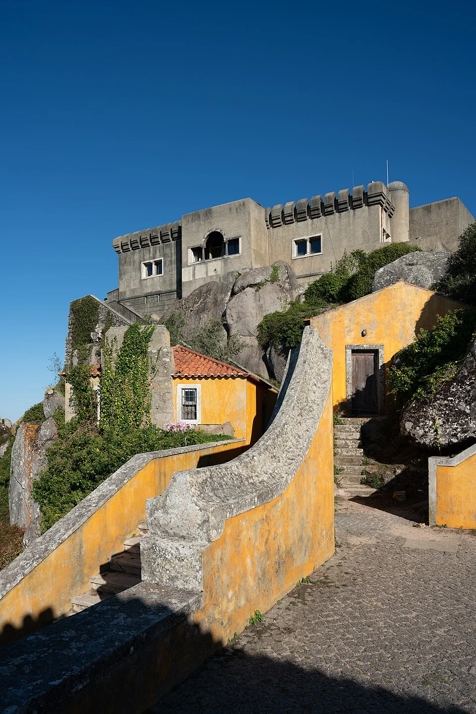 Escaleras de muros amarillos que ascienden entre grandes rocas hasta el Santuario da Peninha, en la sierra de Sintra.