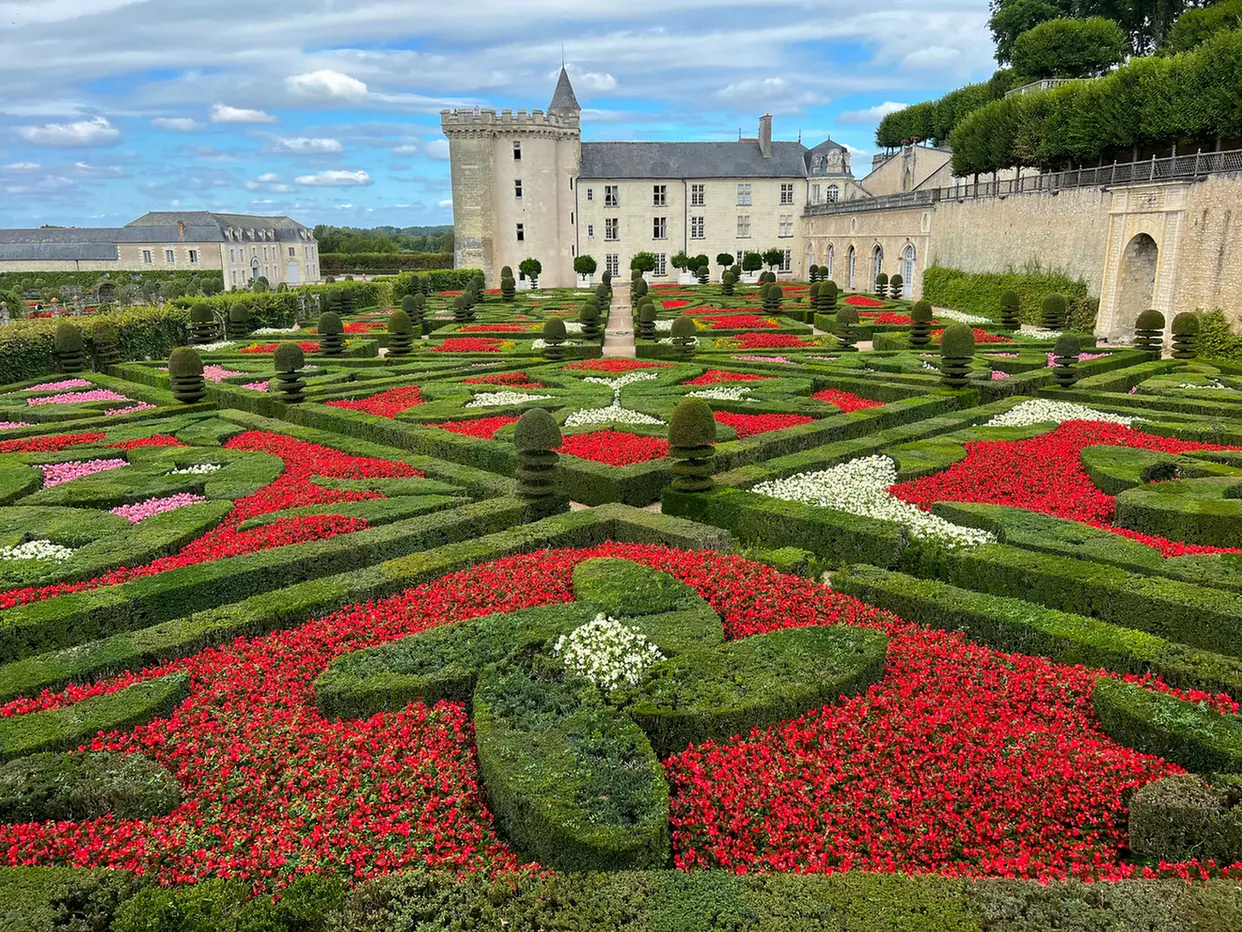 Jardines del Amor del castillo de Villandry, con parterres geométricos de flores rojas, rosas y blancas frente al edificio.